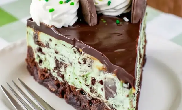 Desserts To Make — close-up of a slice of Thin Mint Cheesecake showing a mint-green cheesecake layer over a chewy brownie crust, glossy chocolate topping, and chopped mint-cookie garnish.