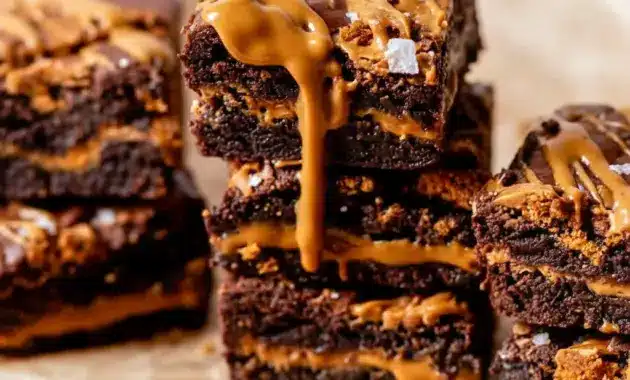 Biscoff Cookie Butter Brownies sliced into squares, revealing a rich chocolate layer, a creamy cookie-butter core, and crushed Biscoff cookies on top.