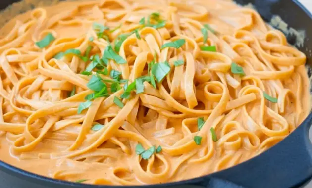 Plate of Red Pepper Alfredo Pasta — creamy red sauce coating fettuccine with a basil garnish, close-up overhead shot.