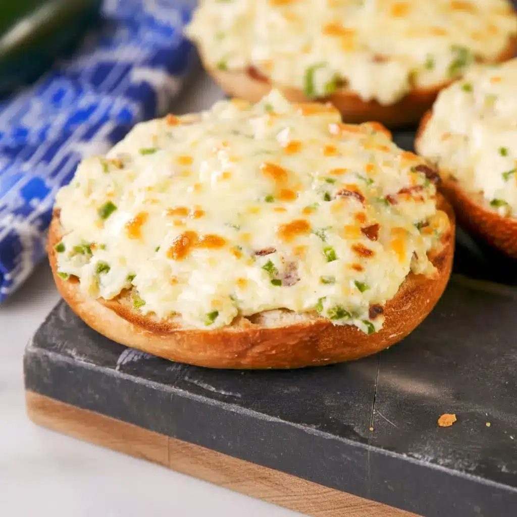 Close-up of baked Jalapeño Popper Bagels — bagel halves spread with jalapeño cream cheese, melted Monterey Jack, and bacon crumbles, garnished with thin jalapeño slices.