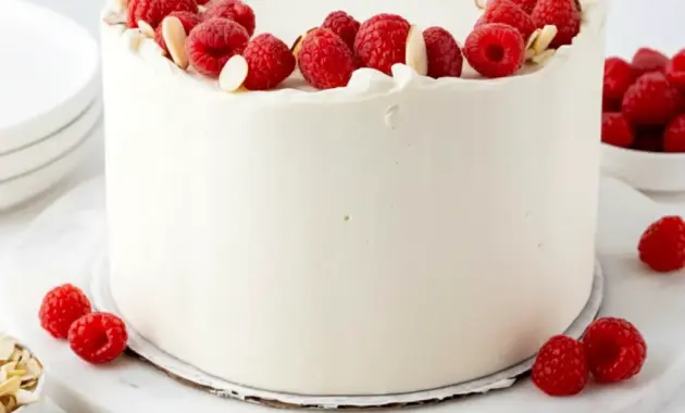 Raspberry Almond Cake with white almond cake layers, raspberry filling, creamy frosting, fresh raspberries, and slivered almonds on top.