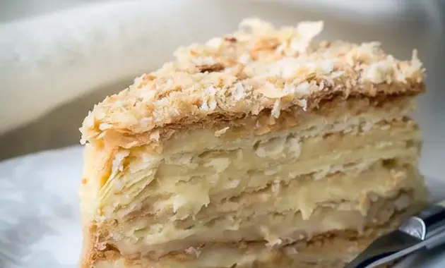 Russian Napoleon Cake slice with thin flaky pastry layers, rich custard filling, and a crumb-coated top on a serving plate.
