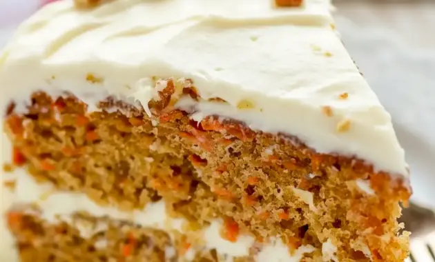 A beautifully layered Carrot Cake Recipe with fluffy Cream Cheese Frosting, featuring a thick slice that shows its tender crumb and rich texture. This Super Moist Carrot Cake is decorated with smooth frosting and simple carrot garnish, making it the perfect Easter Dessert or classic homemade cake for celebrations.