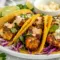 A platter of Blackened Fish Tacos with dark spice-crusted fish, shredded cabbage, lime wedges, and creamy sauce, styled as one of the best Easy Seafood Taco Recipes.