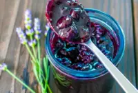 A jar of Blueberry & Lavender Jam with a spoon beside it, styled as a beautiful Homemade Lavender Jam Recipe for toast and gifting.