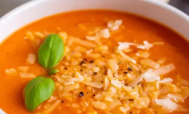 A bowl of High Protein Tomato Soup topped with basil and parmesan, styled as a comforting Creamy Healthy Soup.